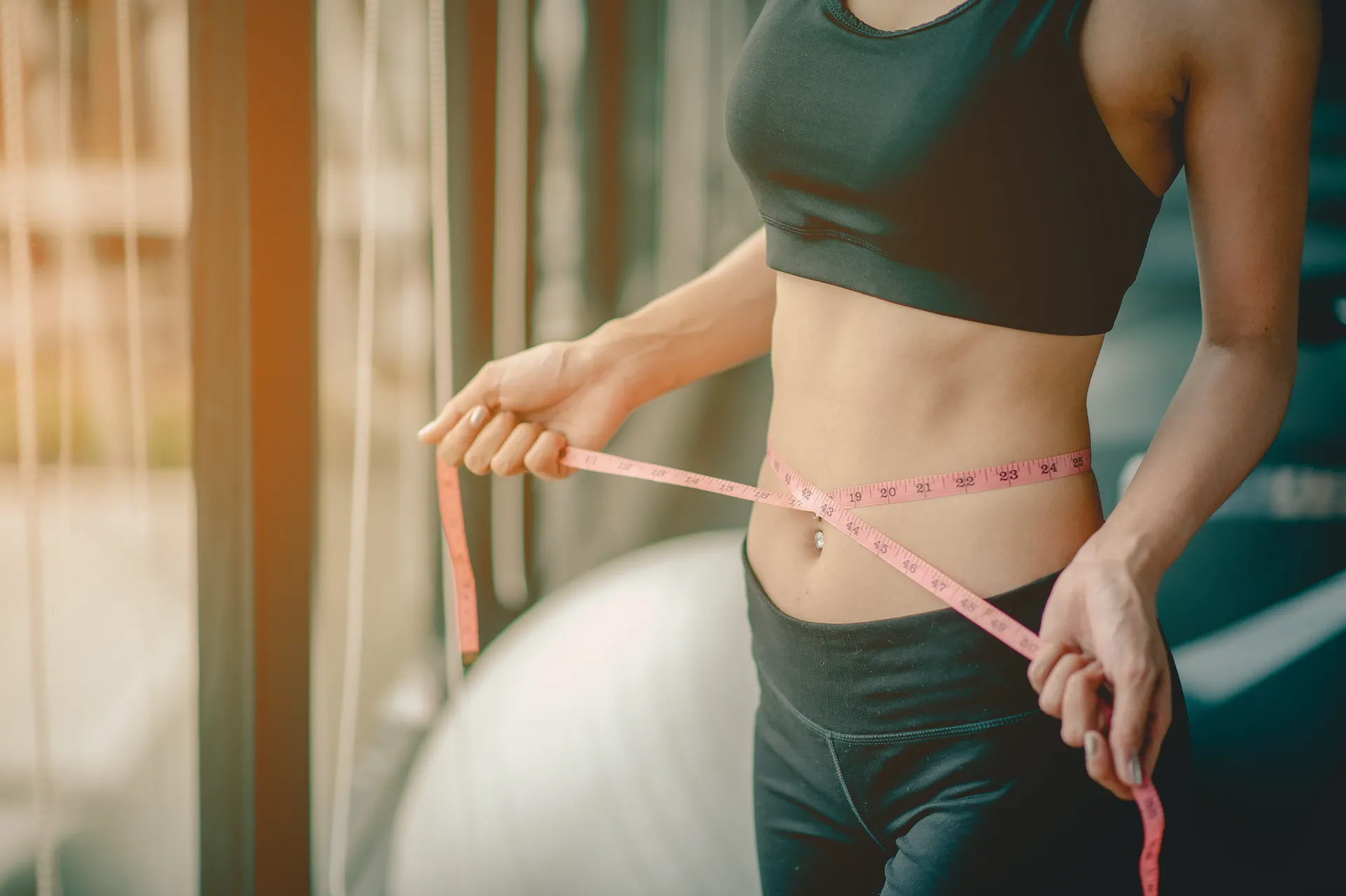 woman measuring waist in gym with pink tape utc